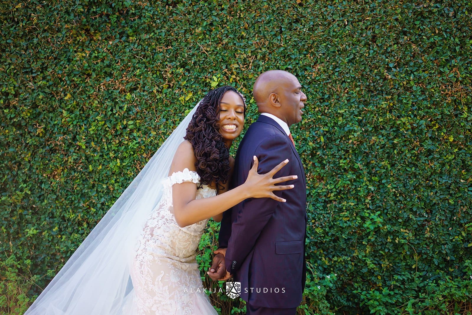 First look with dad — bride hugs her father in front of a large green hedge