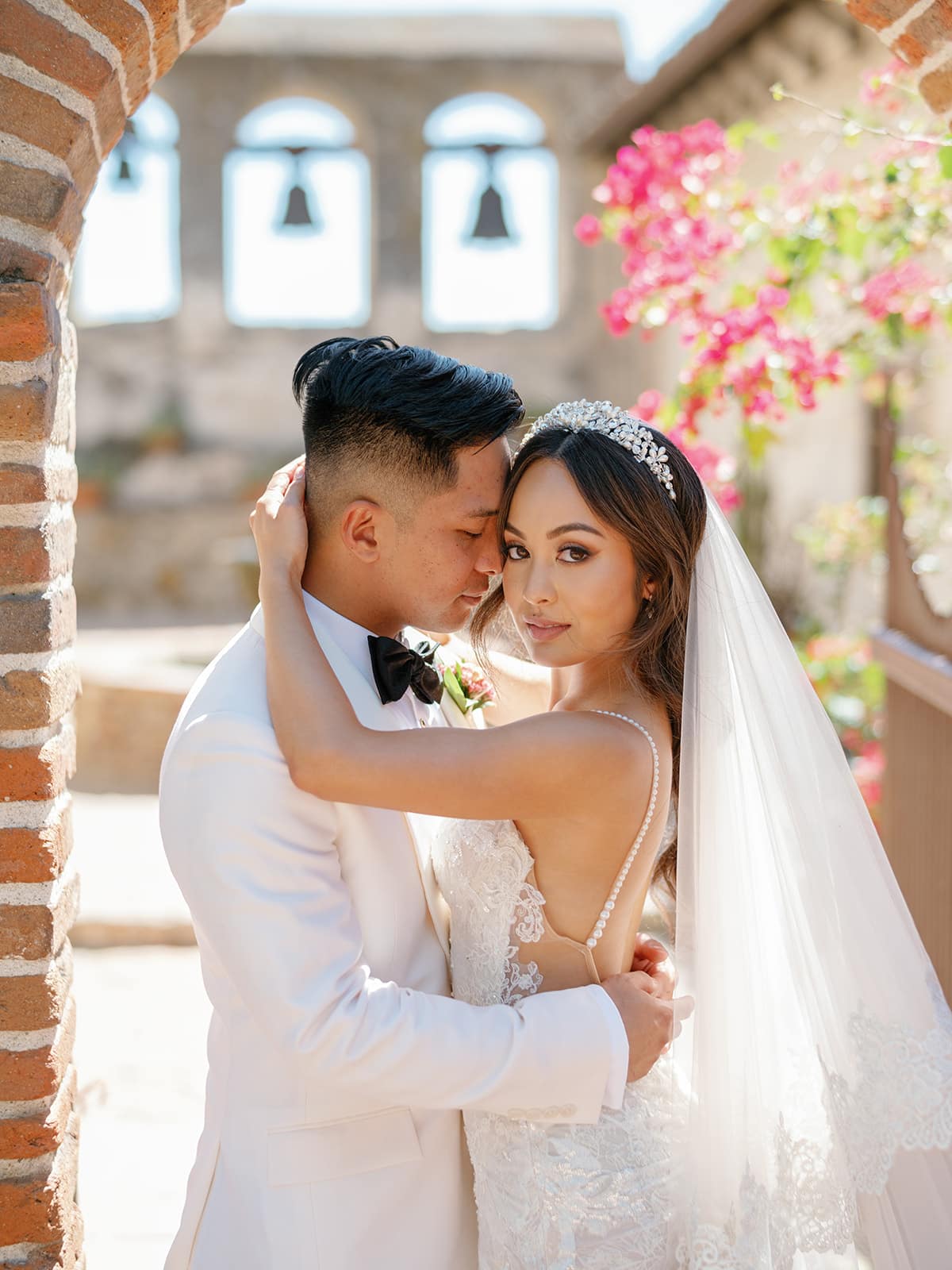 Close-up of a bride and groom embracing with the bride locking eyes with the camera and a touch of pink florals framing them